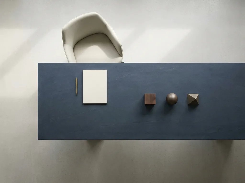 Lege stoel aan het hoofd van een minimalistische vergadertafel met notitieboek en geometrische objecten in ivoor, leisteenblauw en messing.